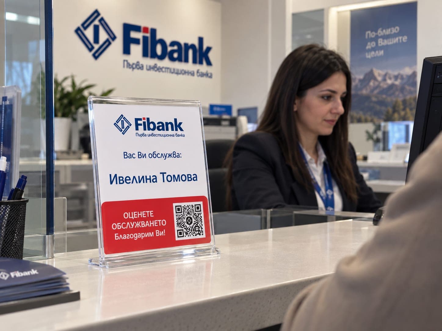 A “Serving you today” nameplate with a QR code on a Fibank counter